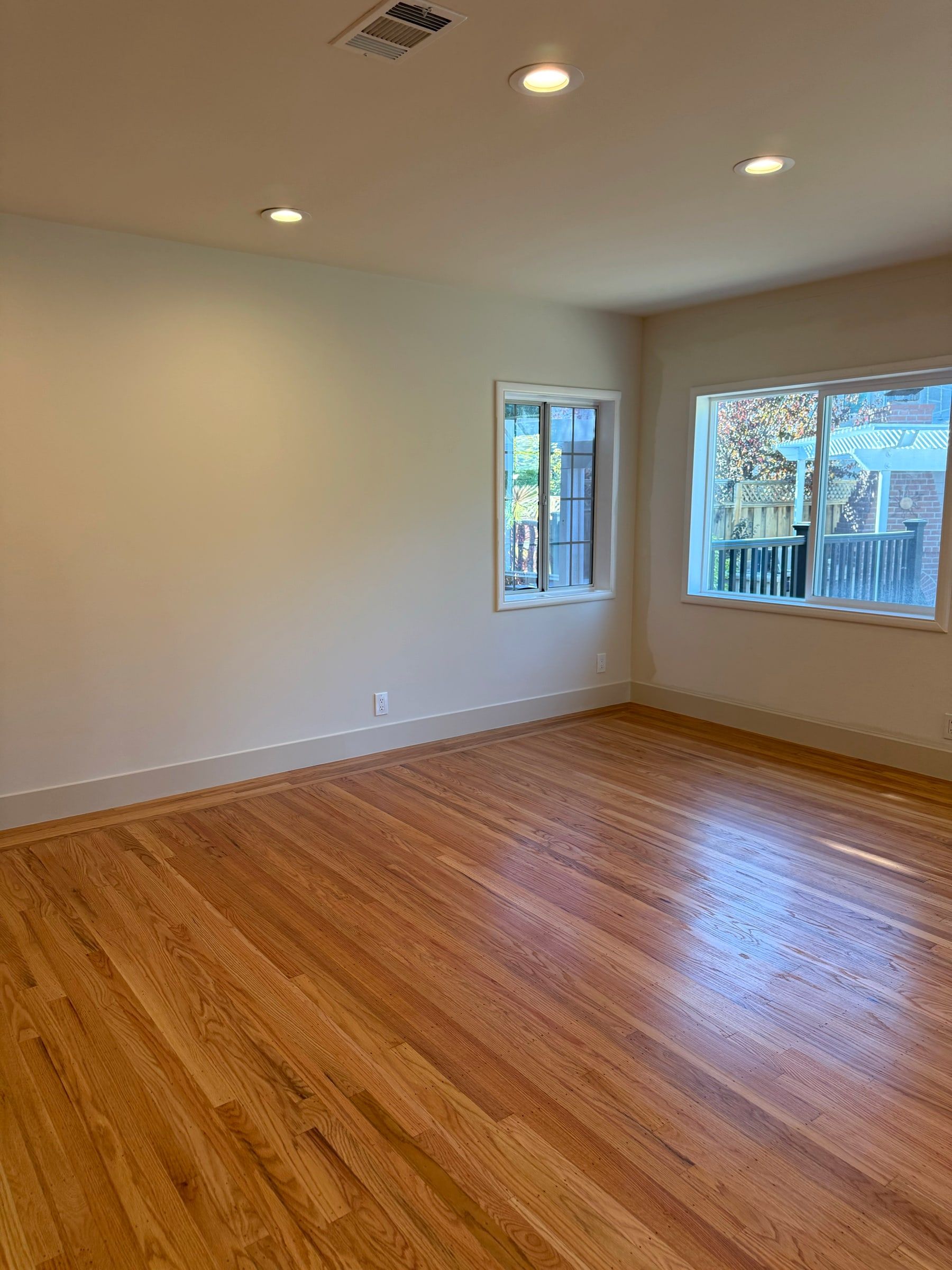 A bright, empty room with gleaming oak floors and sunlight through the windows, freshly cleaned
