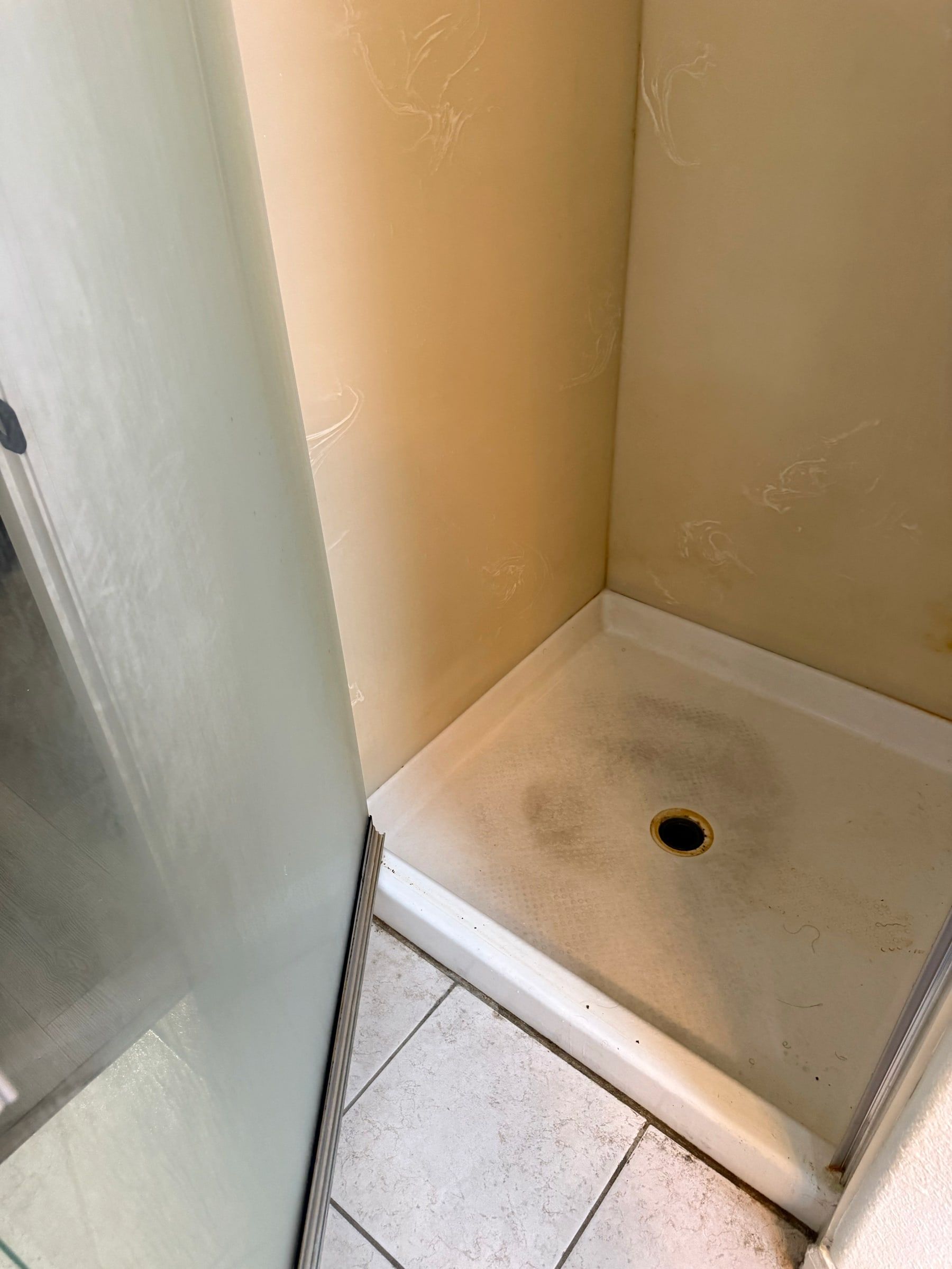 Before: Shower base with dark stains and buildup before deep cleaning